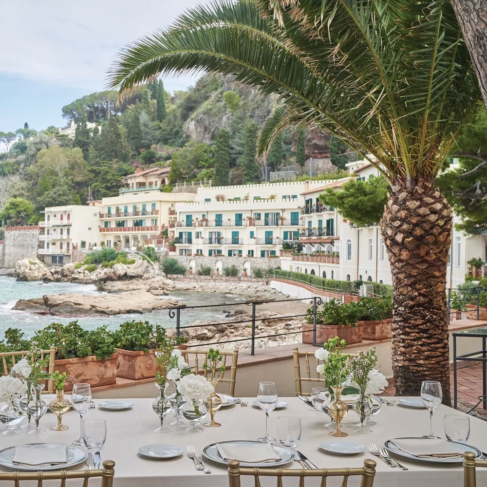 Elegant clifftop wedding table set with white roses and gold chairs overlooking the Mediterranean coastline