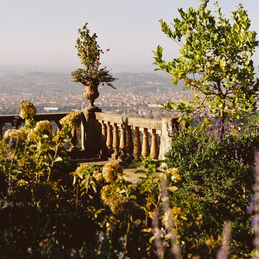 Stone balustrade terrace overlooking a hazy valley town, framed by lavender and hydrangeas