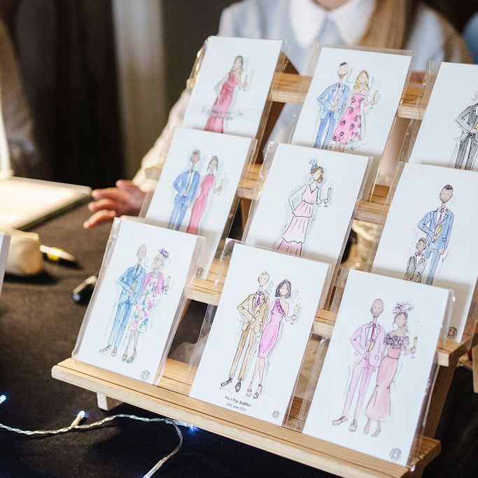 Watercolour illustration cards of couples displayed on a wooden tiered stand at a wedding fair