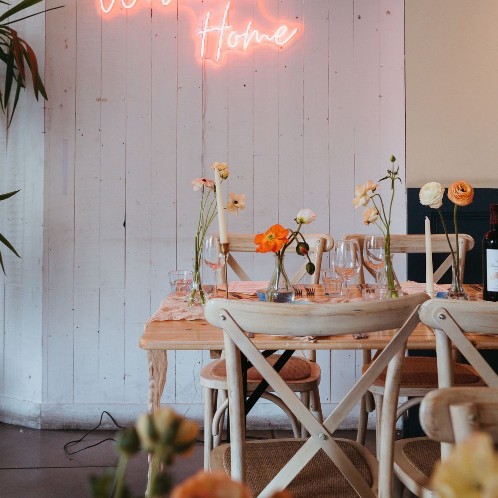 Pink neon 'Welcome Home' sign above a wooden table set with poppies and taper candles