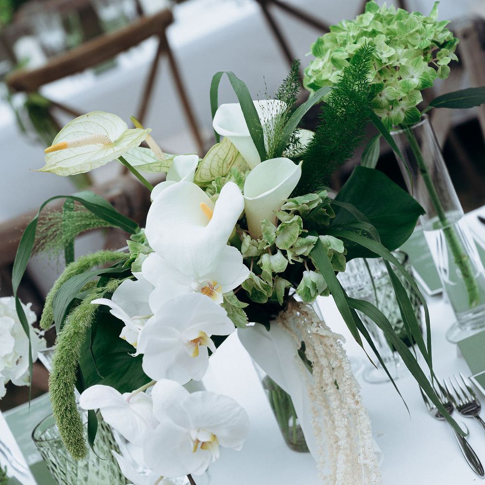 White orchid and green hydrangea centrepiece with trailing amaranthus on a linen-dressed table