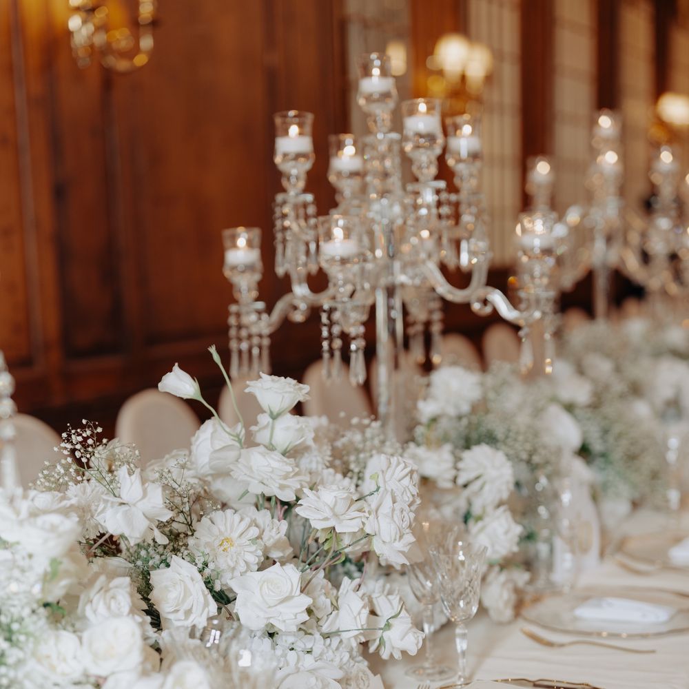 White rose and gypsophila runner along a long banquet table with gold-rimmed chargers and crystal candelabras