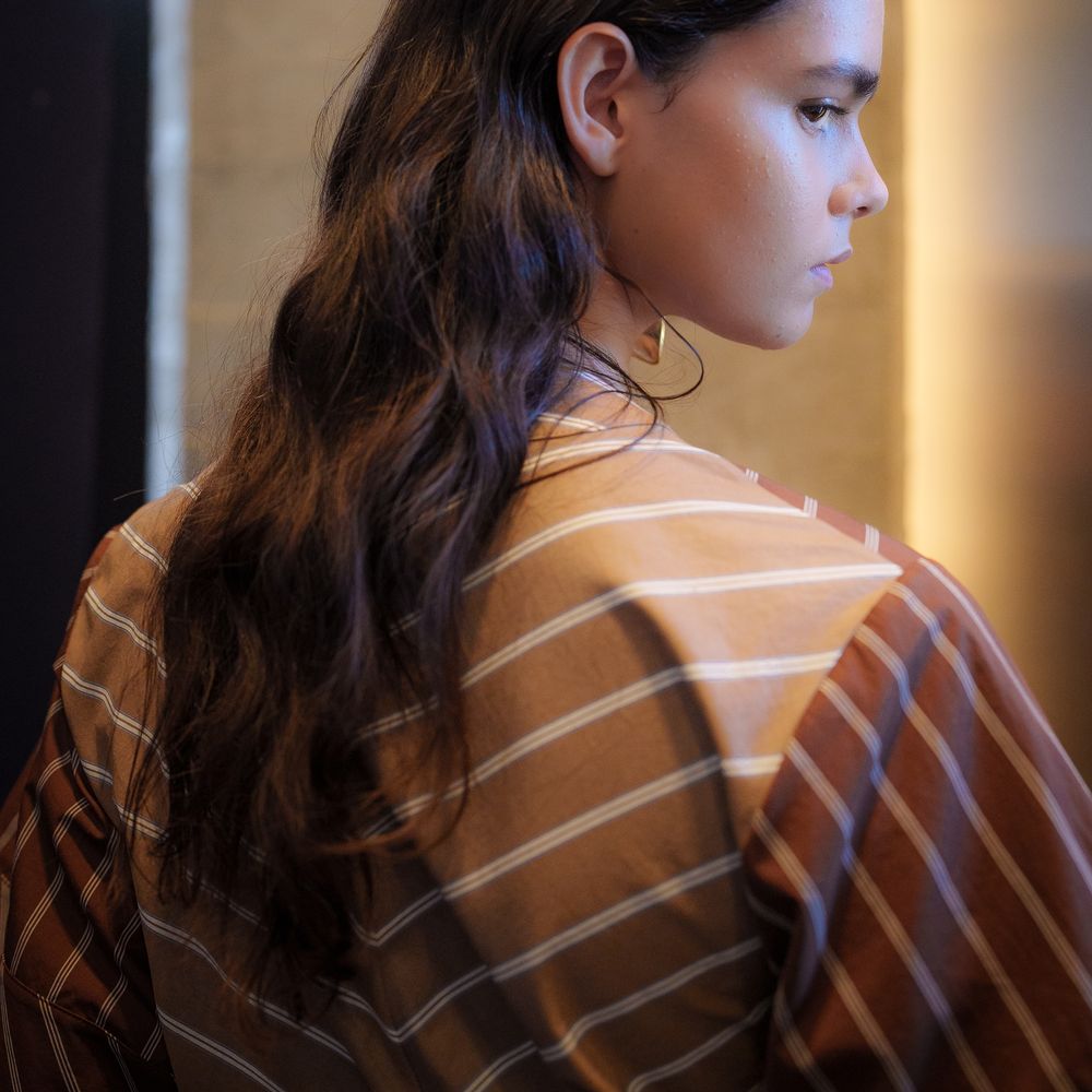 Woman in profile with long wavy hair and a striped rust-toned shirt in warm light