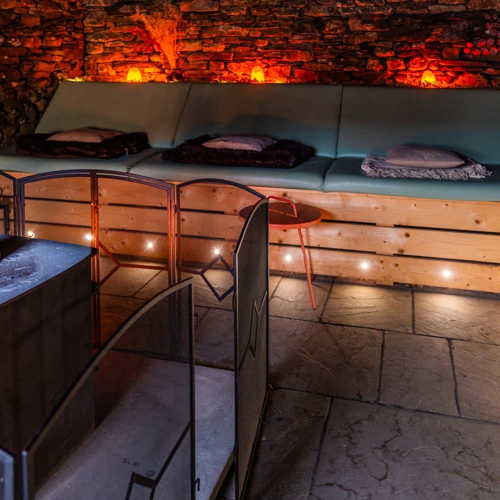 Lit wood burning stove beside a cushioned bench seat against a glowing stone wall