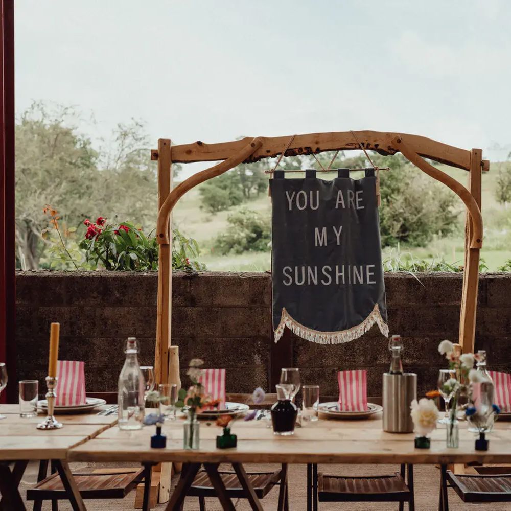 Rustic trestle table with 'You Are My Sunshine' banner on a wooden arch overlooking countryside