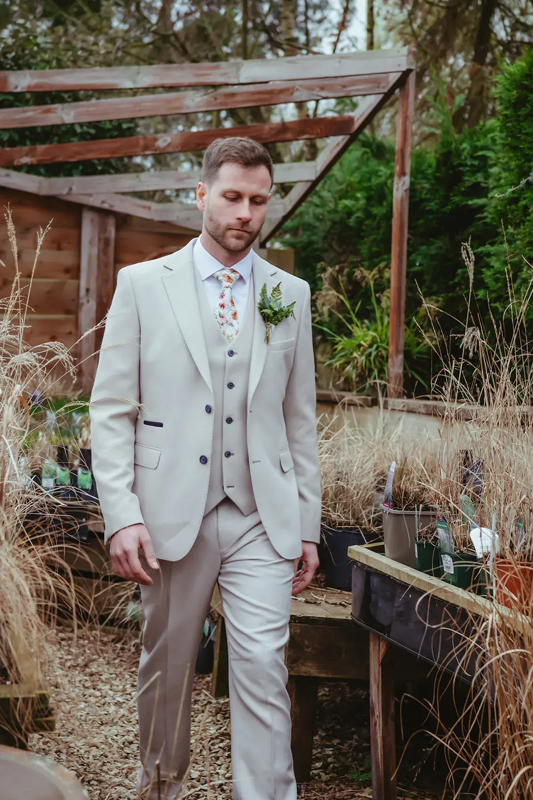 Groom in three piece light grey wedding suit with floral patterned tie with foliage buttonhole accessory 