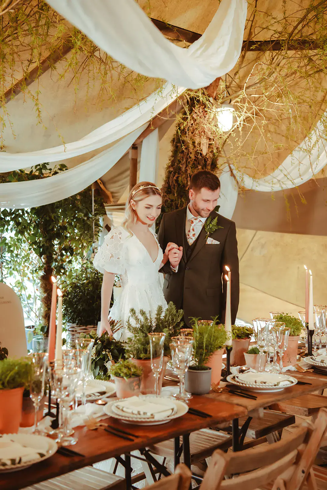 White drapery decorations at The Garden Tipi wedding venue with lots of natural foliage with the bride in floral lace wedding dress and groom in brown wedding suit 