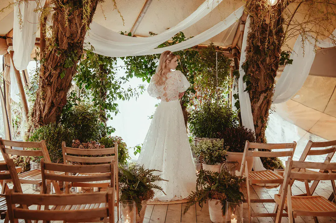 Bride in short sleeve floral lace wedding dress from Love And Loved Bridal with foliage and white drapery decorations 