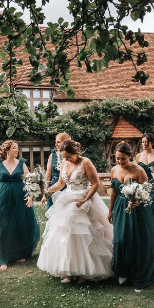 Bride in layered wedding dress walks with bridesmaids in green bridesmaid dresses
