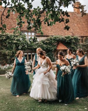 Bride in layered wedding dress walks with bridesmaids in green bridesmaid dresses