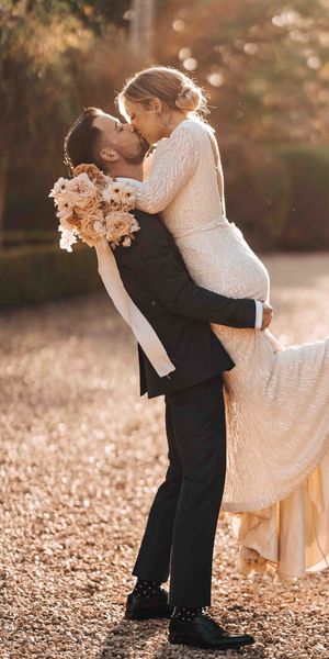 Bride in beaded wedding dress is picked up and kissed by the groom in front of Pennard House wedding venue.