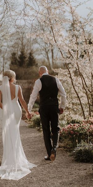 Bride in button back wedding dress from Made With Love walks holding hands with groom around Middleton Lodge for black tie wedding.