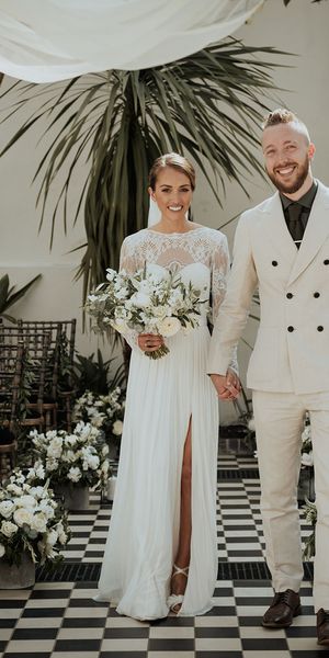 bride in lace Catherine Dean wedding dress with white wedding bouquet stands with husband in beige suit at Gunnesbury Park Orangery wedding altar