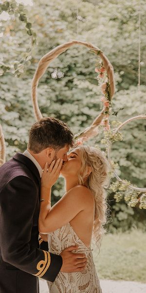 Hula hoop decor for the altar with the bride in a boho lace wedding dress kissing the groom in military uniform. 