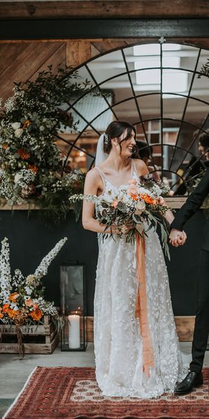 bride in a lace dress and groom in a black tuxedo at new Lake District wedding venue with oval micro back drop and colourful floral arrangements