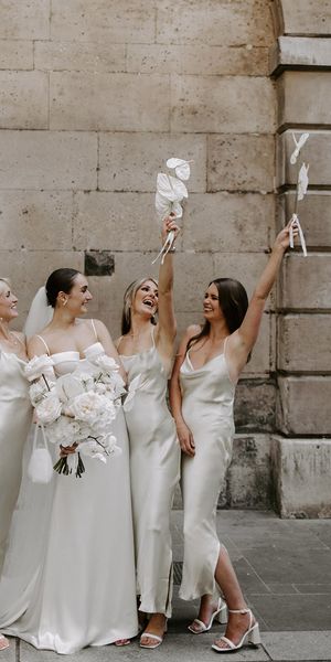 Bride holding white wedding bouquet with bridesmaids in white dresses.