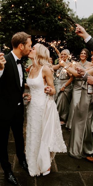 Bride in a 3D applique wedding dress with the groom sharing a kiss for their sparkler send off.