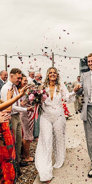fun east quay Whitstable wedding with bride in a jumpsuit, pink & red colour scheme and mismatched bridesmaid dresses