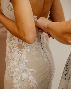 Bride getting help fastening the back of her lace wedding dress