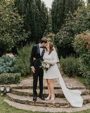 The bride wears a short wedding dress with bow with the from in black tux for wedding.