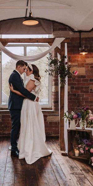 Bowers Mill wedding venue with industrial elements and pretty wildflower decor arranged by the bride herself. Bride wears Jesus Peiro gown and groom wears blue suit.