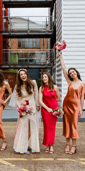 Trinity Buoy Wharf wedding with bride in a lace Rixo dress and bridesmaids in red and orange satin bridesmaid dresses