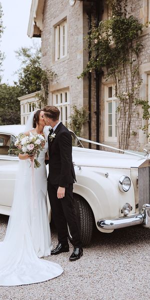 Bride and groom kissing in front of white wedding car at the Casterton Grange Estate venue.