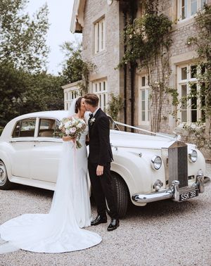 Bride and groom kissing in front of white wedding car at the Casterton Grange Estate venue.