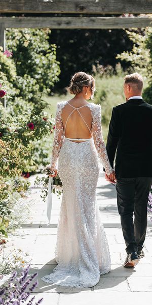 Bride in 3D lace wedding dress with an open back walking with the groom in black tie.