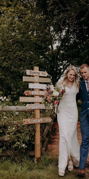 Bride and groom in front of their DIY wedding sign for rustic wedding at barn venue.