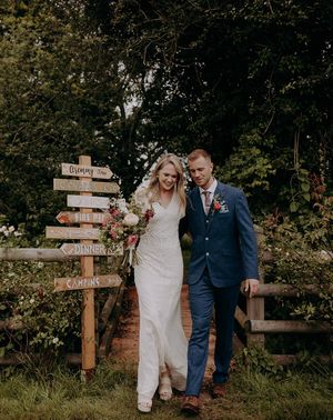 Bride and groom in front of their DIY wedding sign for rustic wedding at barn venue.