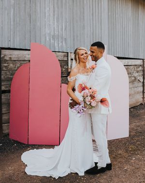 Bride and groom laugh together in front of their DIY pink wedding screen background.