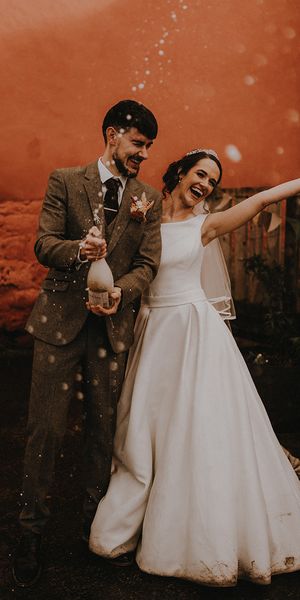 Rustic romance wedding theme for Devon wedding with the bride and groom popping champagne.