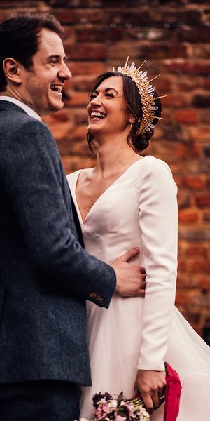 Bride in gold and crystal bride crown in layered wedding dress with groom in navy suit.