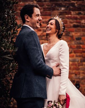 Bride in gold and crystal bride crown in layered wedding dress with groom in navy suit.