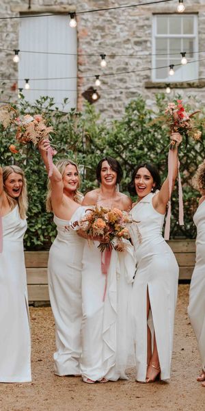 Bride in Alexandra Grecco dress with bridesmaids in white one shoulder dresses and neutral wedding bouquets.