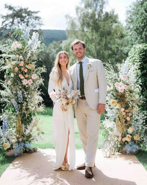 Bride wearing custom Bon Bride gown with plunging neckline and front slit with groom in cream suit in front of pastel flower displays for garden tipi wedding