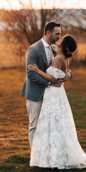 Bride in floral lace wedding dress with groom in grey suit share a kiss before their mariachi band wedding entertainment.