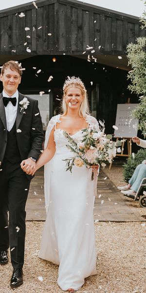 Bride in handmade wedding dress with crown walking with groom in black tie. 