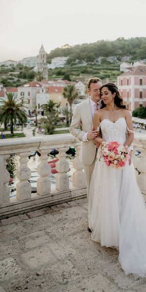 bride and groom stand on a balcony with Old Town Hvar in the background at destination wedding in Croatia 