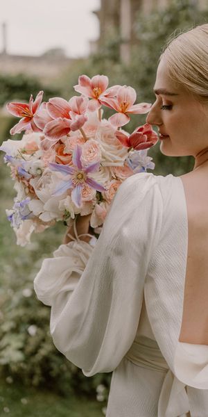 bride-in-open-back-wedding-dress-smelling-pink-wedding-bouquet-with-pearl-earrings