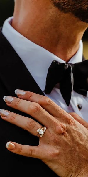 bride's hand on groom's chest with oval solitaire diamond engagement ring and chunky diamond wedding ring