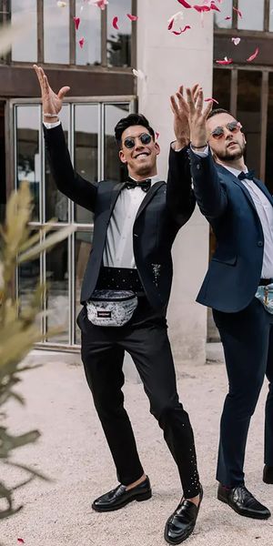 two groomsmen in dark blue suits and black bow ties with fanny packs or bum bags full of petals