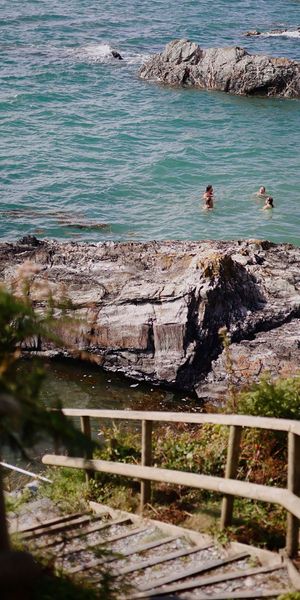 View of people swimming from the steps leading to private beach at Polhawn Fort