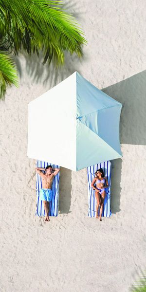 Couple relaxing on a white-sand beach under a parasol at a Sandals Resorts adults-only all-inclusive Caribbean honeymoon destination