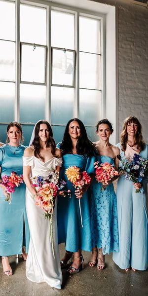 Bridal party wearing mismatched blue bridesmaid dresses with colourful bouquets