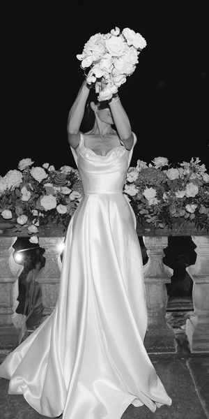 Black and white photo of a bride in a floor-length wedding dress holding a bouquet raised in the air.