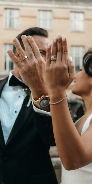 Bride and groom put their left hand up to the camera to show off their new wedding rings and alternative engagement ring