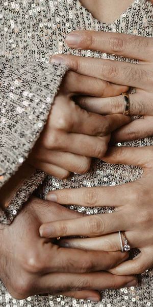 Couple holding hands across silver sparkly wedding dress with engagement rings