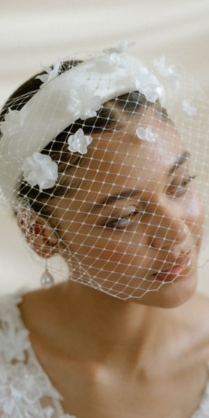 Bride wears an ivory birdcage wedding veil with 3d flowers and an ivory padded headband
